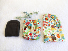 Load image into Gallery viewer, Nappy with a design of a colourful woodland setting, with owl and flowers, in warm red, calming blue and earthy tones.