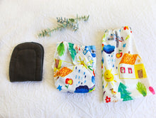 Load image into Gallery viewer, A white background nappy with bright design with a smiling sun, clouds, a little home, plane and trees.