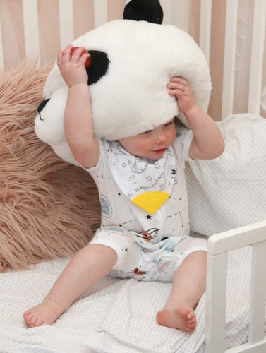 Baby sits with stuffed panda mascot head above her face, in stunning blue, beige and black onesie with Bamboo Babywear bib over the top with yellow teeth tip.
