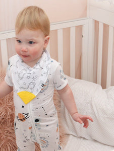 Baby stands in cot, with onesie and bib on.