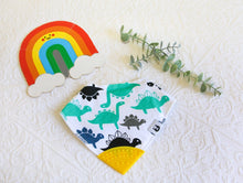 Load image into Gallery viewer, Turquoise, navy, black and grey dinosaurs on a white bib, with a yellow teething tip.