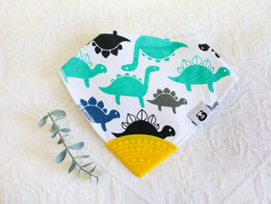 Turquoise, navy, black and grey dinosaurs on a white bib, with a yellow teething tip.