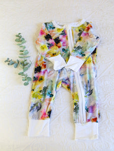 A long sleeved onesie in a stunning water colour style print with vibrant hints of lilac, yellow, orange and pink.