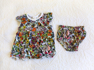 An abundance of vibrant colours on a romper dress with matching knickers. Pattern includes bumblebees, butterflies and flowers in yellows, oranges, purples and pinks all in black outlines.