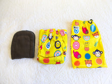 Load image into Gallery viewer, Bold designed nappy, in sunshine yellow with cartoon animal faces including a monkey, giraffe and elephant, amongst others. 