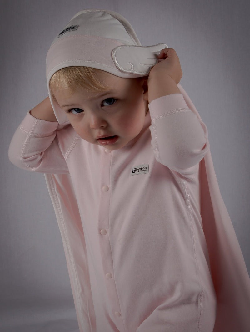 Toddler wears blush pink onesie with towel resting on her head as a cape.