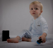 Load image into Gallery viewer, Little boy sat in a lovely baby blue onesie holding a small toy out. 