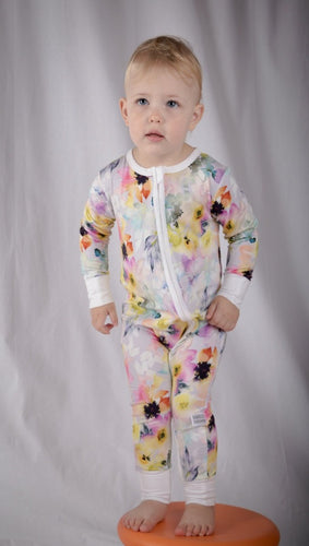 Baby stood on orange cushion, wearing beautiful water colour onesie