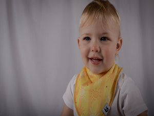 Baby smiles wearing a bright and warm toned yellow, orange and white bi with sunshine pattern.