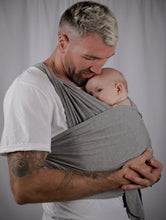 Load image into Gallery viewer, Image of a man holding a baby, with a charcoal grey baby carrier supporting the baby against the mans chest. 